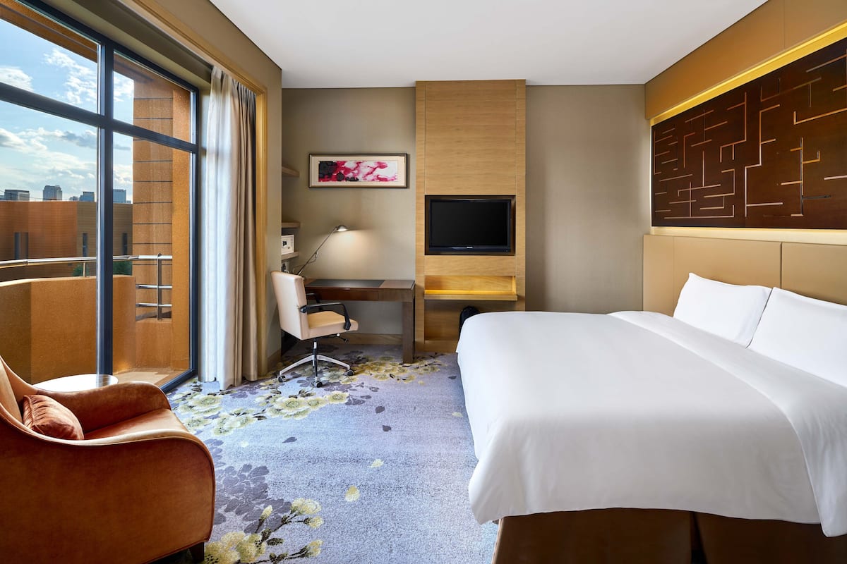 A hotel room with a large bed, a desk with a chair, a TV, and a window with curtains.