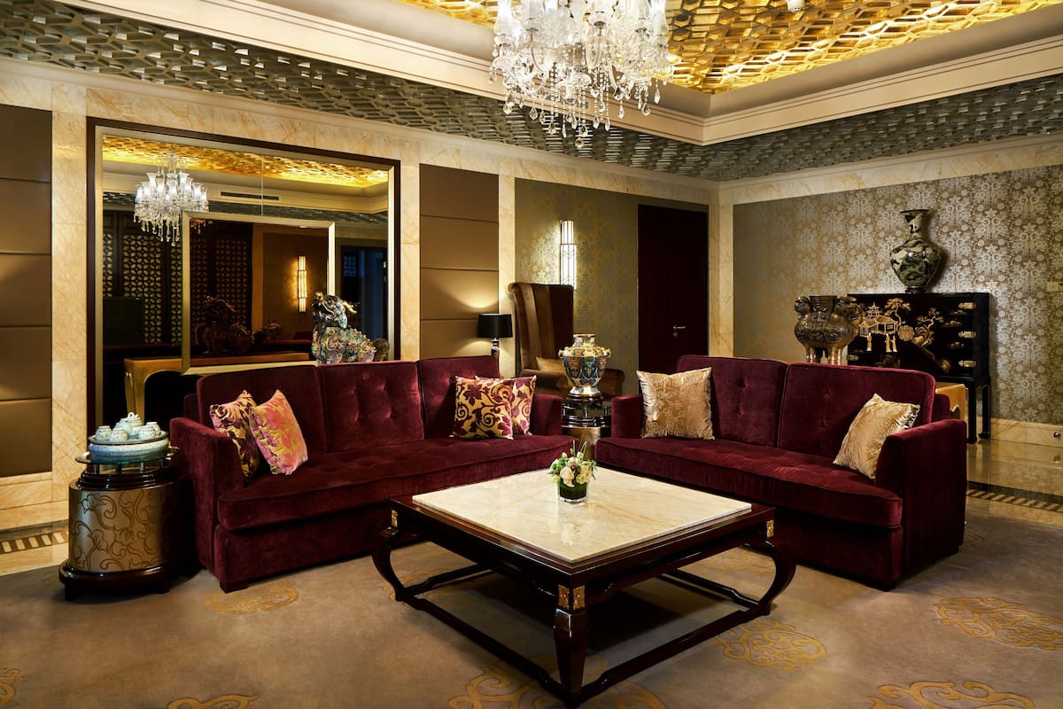 A luxurious living room with a large red sofa, a marble coffee table, and a chandelier.