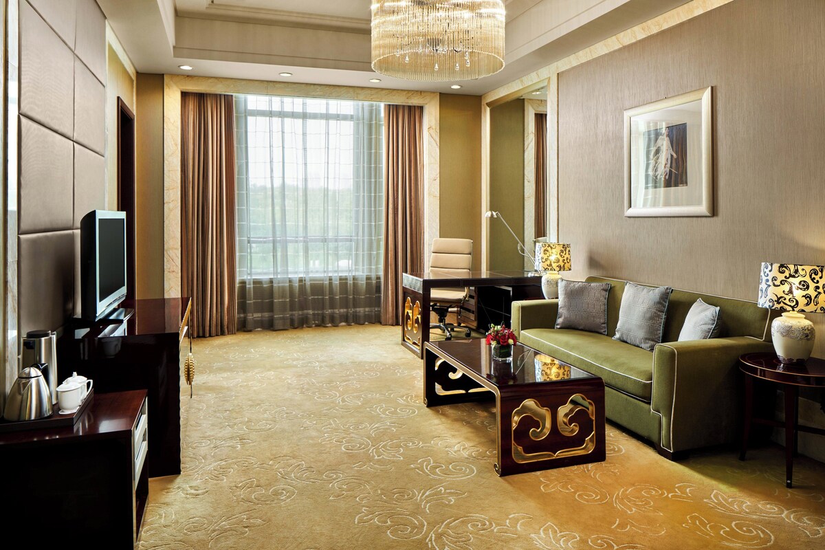 A hotel room with a television, sofa, coffee table, and a large window with curtains.