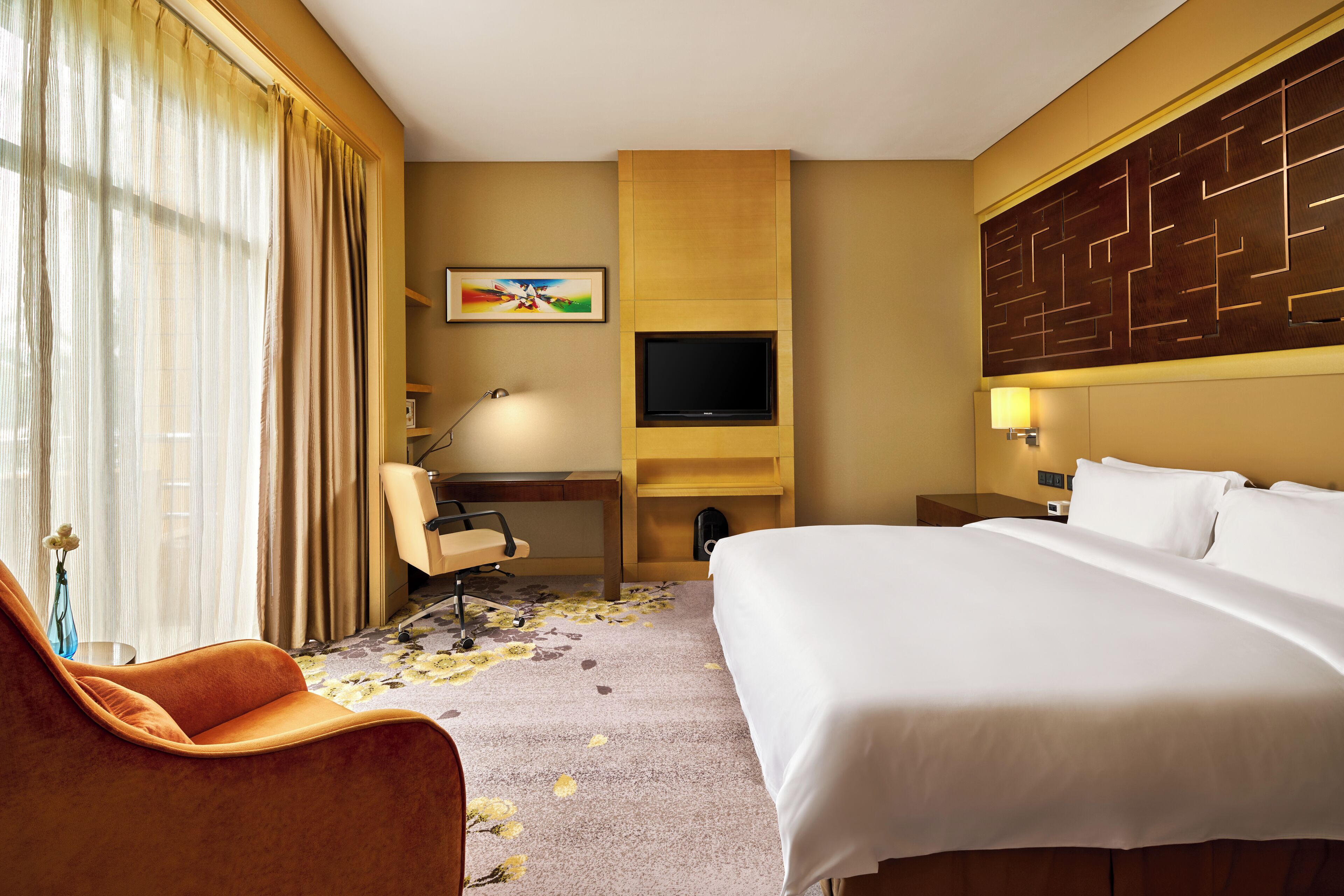 A hotel room with a bed, a desk, a chair, a television, and a wall-mounted artwork.