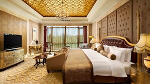 A luxurious hotel room with a large bed, a television, a sofa, and a dining table.