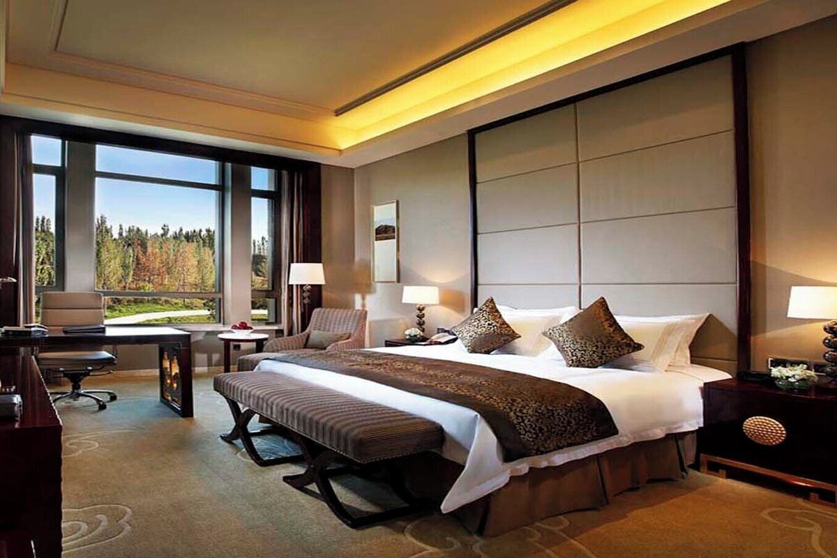 A hotel room with a large bed, a desk, a chair, a television, and a view of the outdoors.