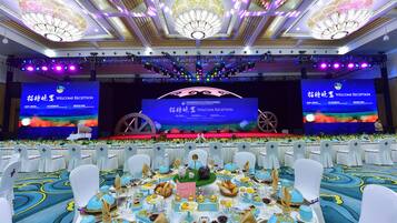 Un salón de banquetes con escenario, mesas dispuestas para una recepción y una pantalla grande que muestra el texto "WELCOME RECEPTION".