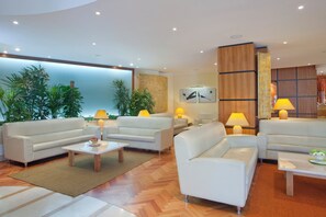 A modern living room with white sofas, a coffee table, and lamps. There are plants and artwork on the walls. - Holiday Inn Cagliari by IHG (Cagliari)