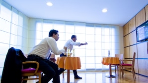 A modern room with large windows, two tables with orange tablecloths, and a television mounted on the wall. - Holiday Inn Cagliari by IHG (Cagliari)