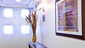 A hallway with a wooden console table holding a vase with dried plants, a framed artwork on the wall, and a door with frosted glass panels. - Holiday Inn Cagliari by IHG (Cagliari)