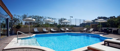 Una piscina en la azotea con sillas de descanso y sombrillas.