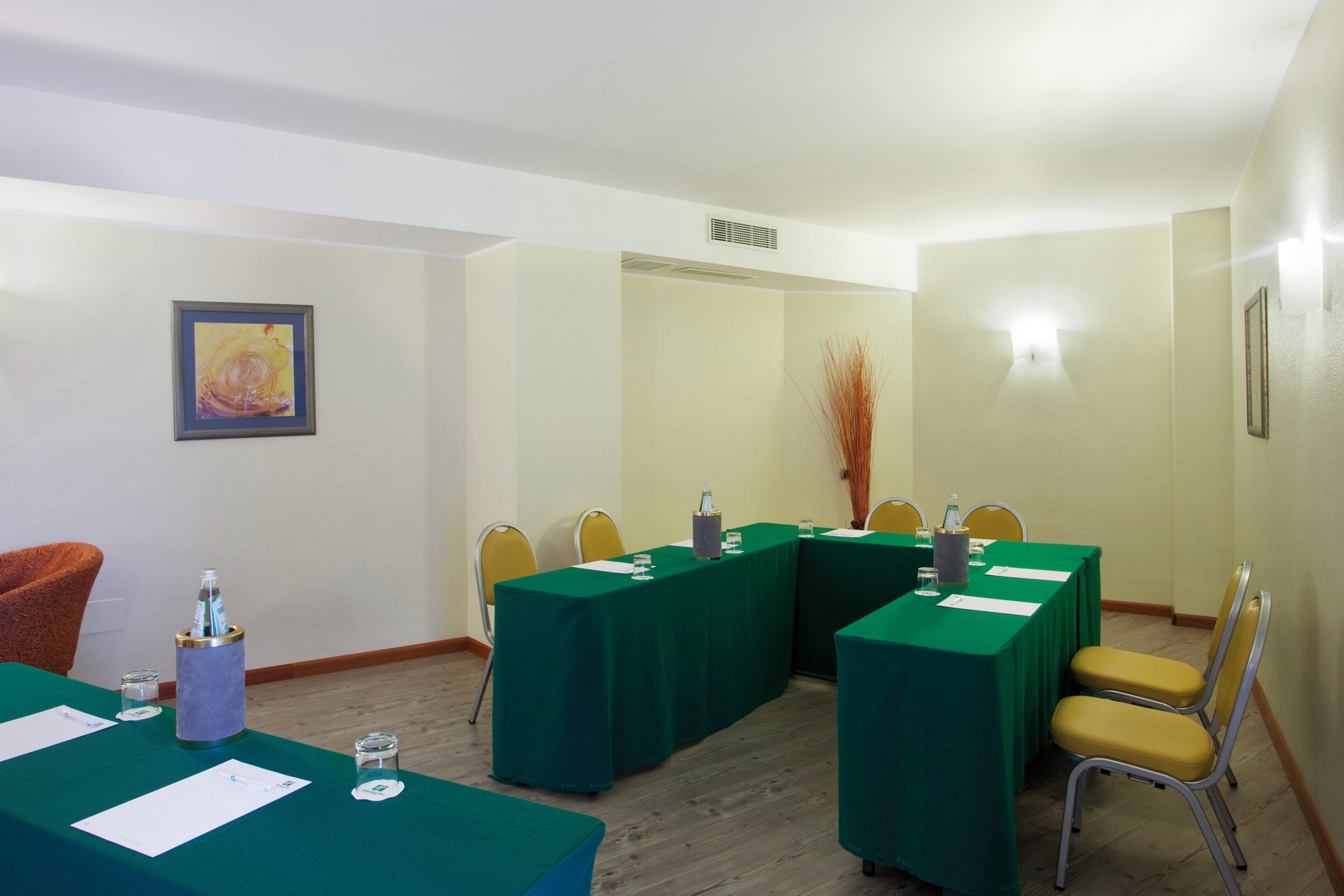 Un salón de conferencias con mesas verdes, sillas amarillas y un cuadro abstracto enmarcado en la pared.