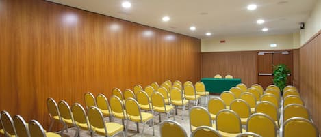 A conference room with rows of yellow chairs, a green table, wooden panel walls, and ceiling lights.