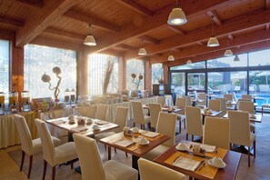 A spacious dining area with multiple tables and chairs, large windows, and a view of the outdoors.