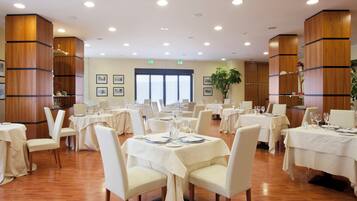 Un vaste espace dédié à la salle à manger, avec plusieurs tables dressées pour le repas, nappes blanches et chaises assorties.