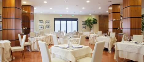 A spacious dining area with multiple tables set for dining, featuring white tablecloths and chairs.
