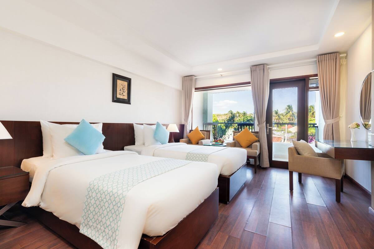 A hotel room with two beds, a desk, and a view of the outdoors.