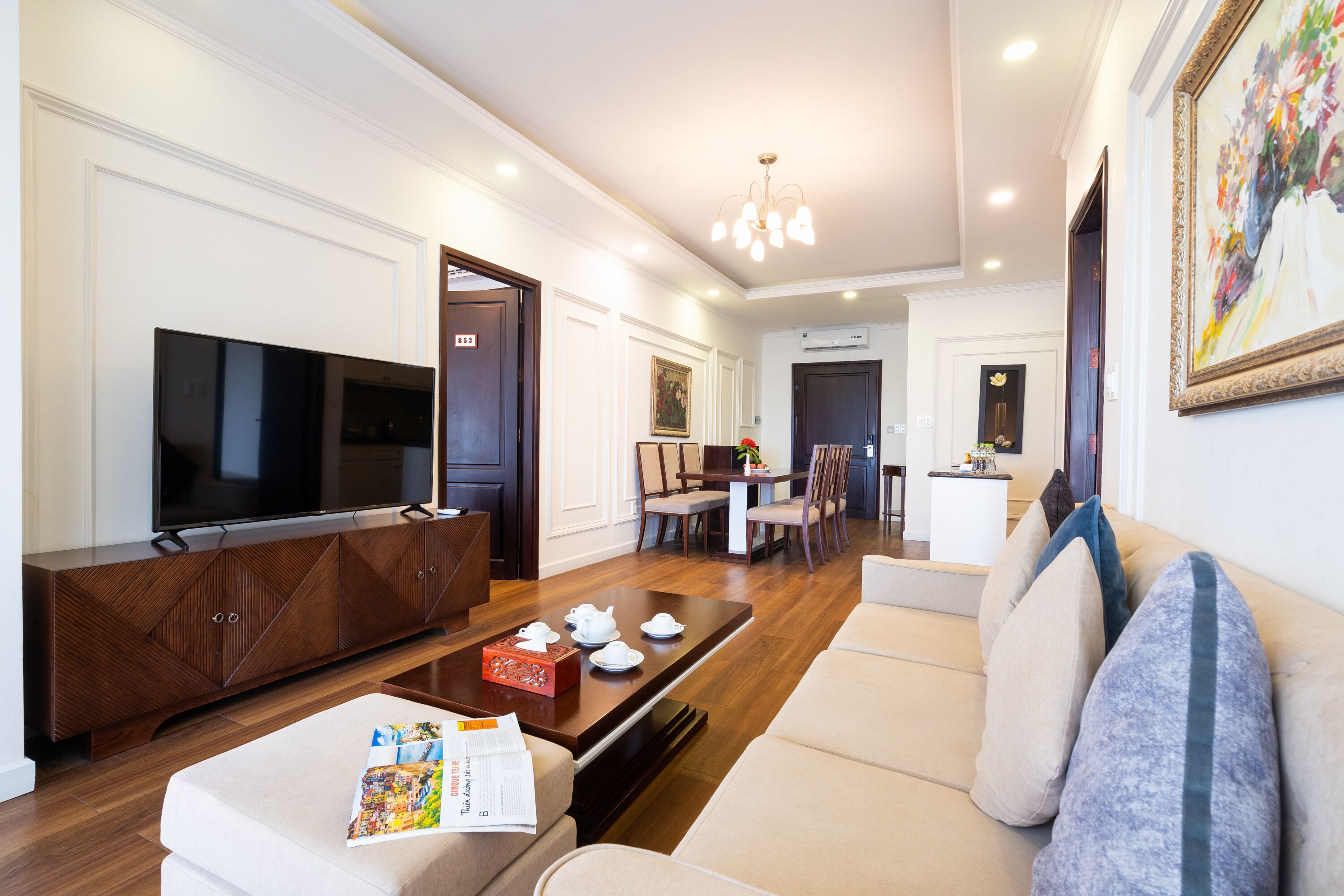 A modern living room with a flat-screen TV, wooden entertainment unit, and a dining area with a table and chairs.