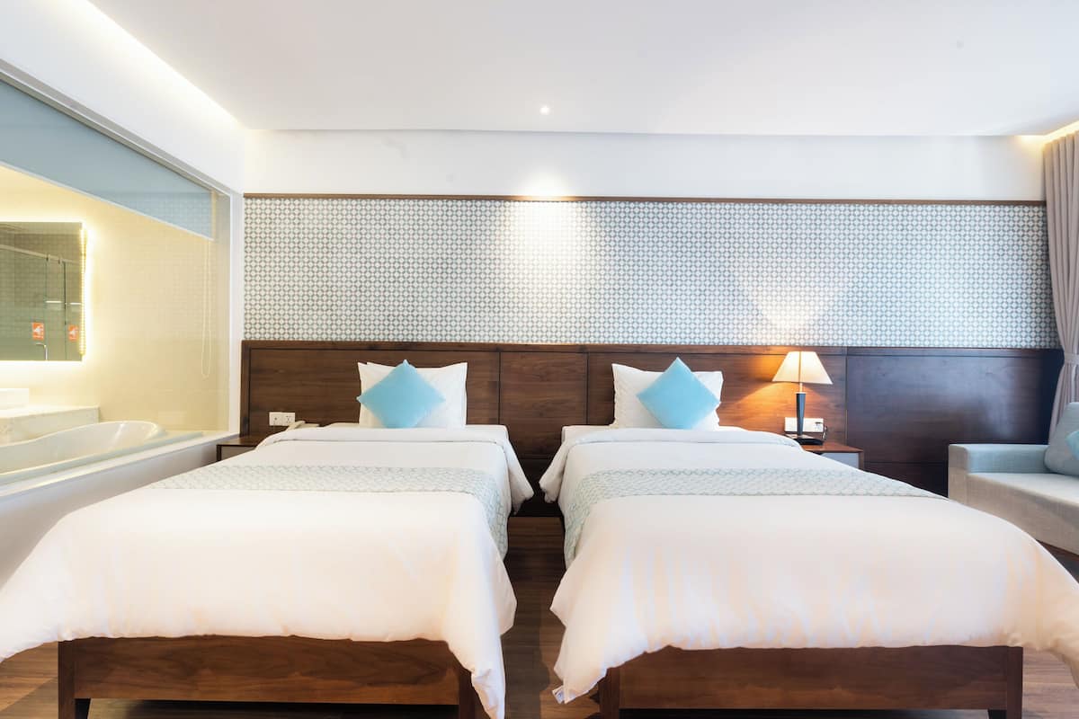 A hotel room with two beds, a large mirror, a bathtub, and a patterned wall.