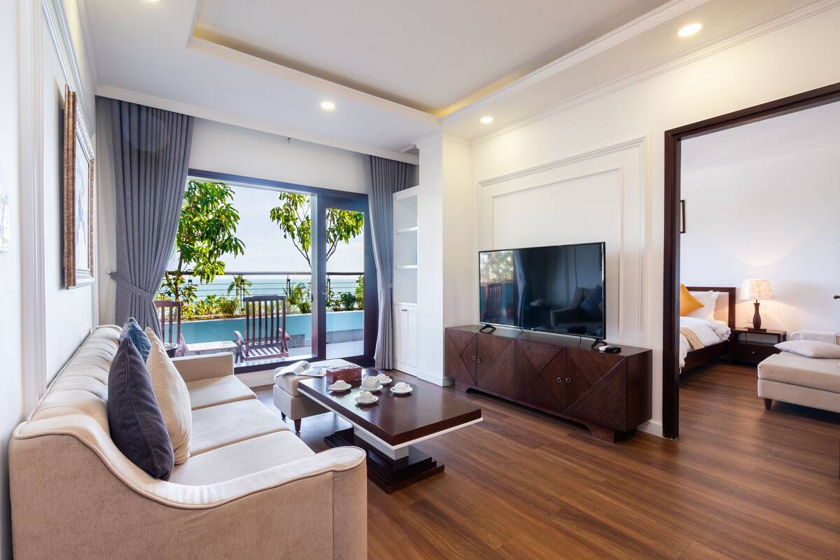 A modern living room with a sofa, coffee table, TV, and a balcony with a view.