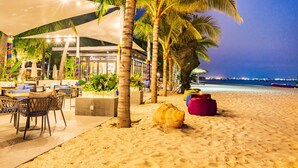 Un restaurante frente al mar con mesas al aire libre, palmeras y vistas al océano.