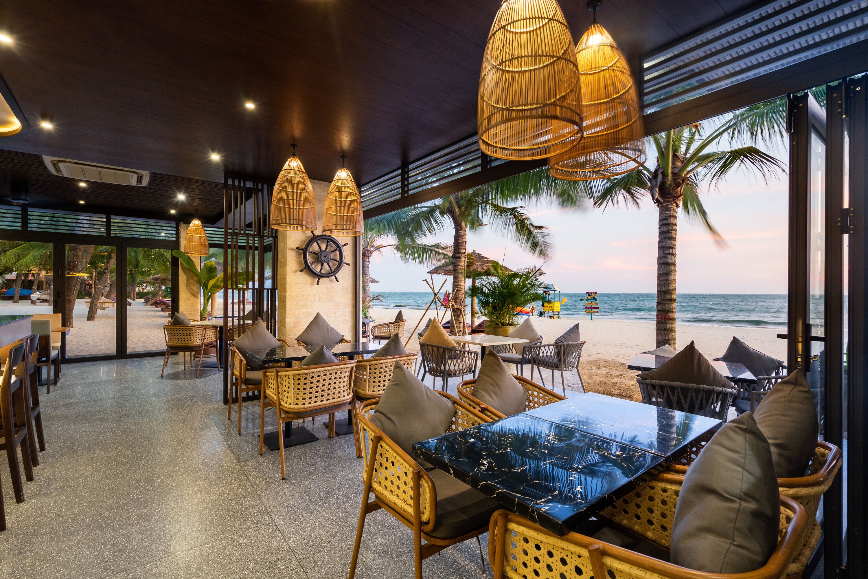An indoor seating area with wicker furniture, a large table, and a view of the beach.