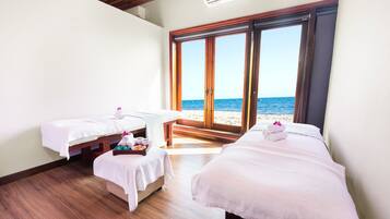 A room with two beds, a small table with a tray of snacks, and a view of the beach through large sliding doors.