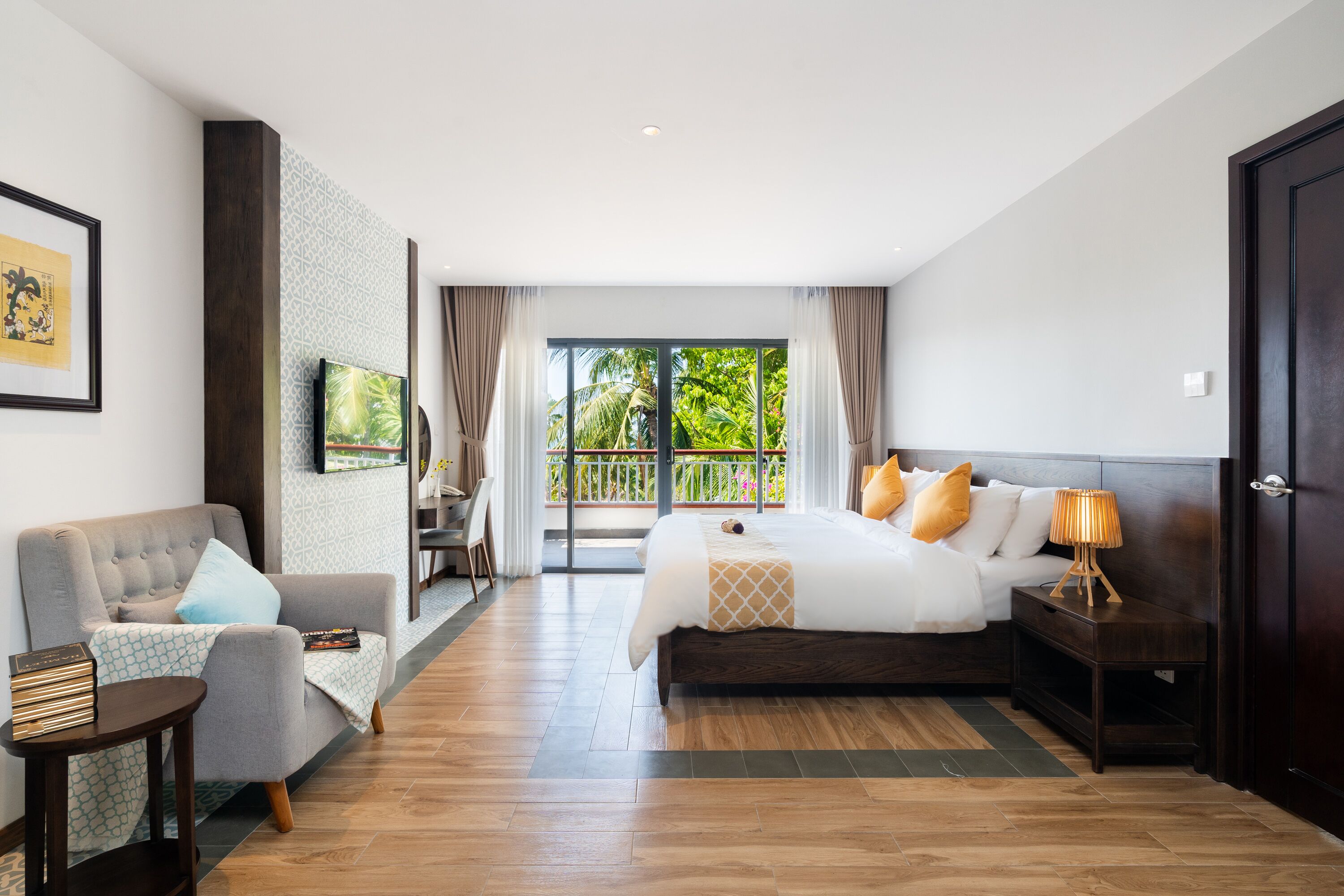 Een hotelkamer met een bed, een slaapbank, een televisie en een balkon met uitzicht op groen.