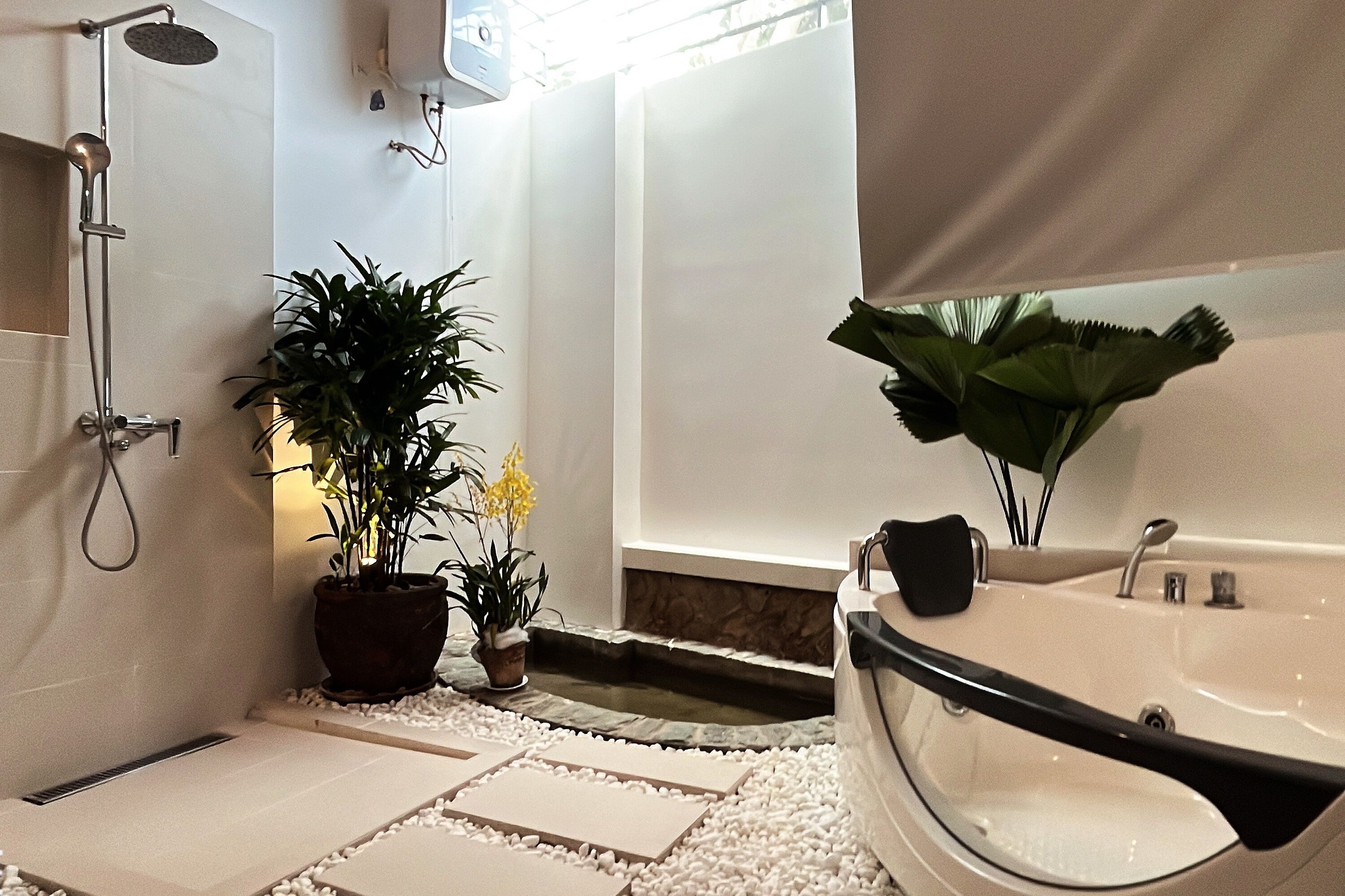 A modern bathroom with a bathtub, shower, potted plants, and a small water feature.