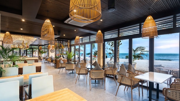 Un espacio interior amplio con mobiliario de mimbre, ventanas grandes con vistas a la playa y lámparas colgantes de mimbre.