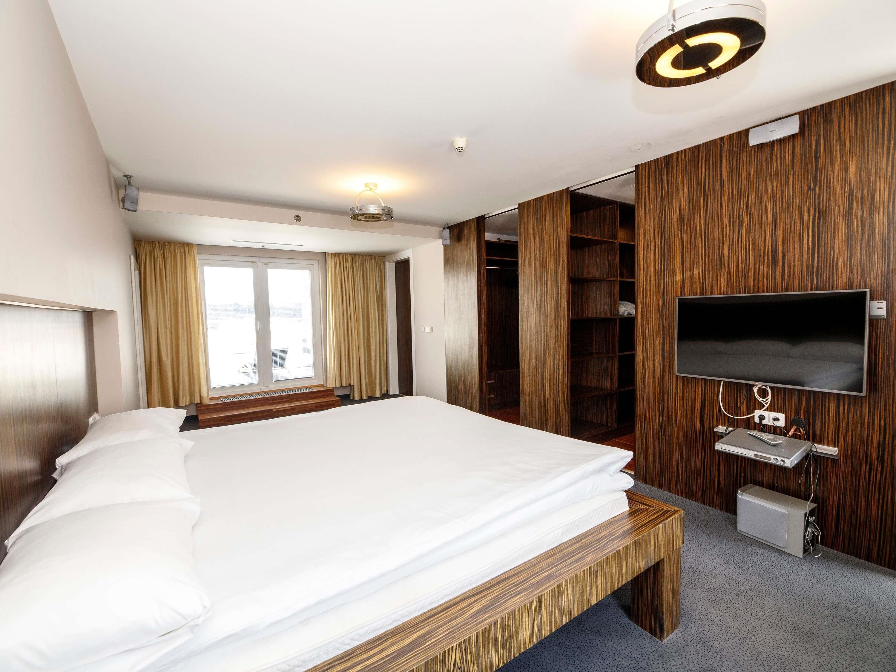 A hotel room with a large bed, a TV mounted on the wall, and a wooden wardrobe.