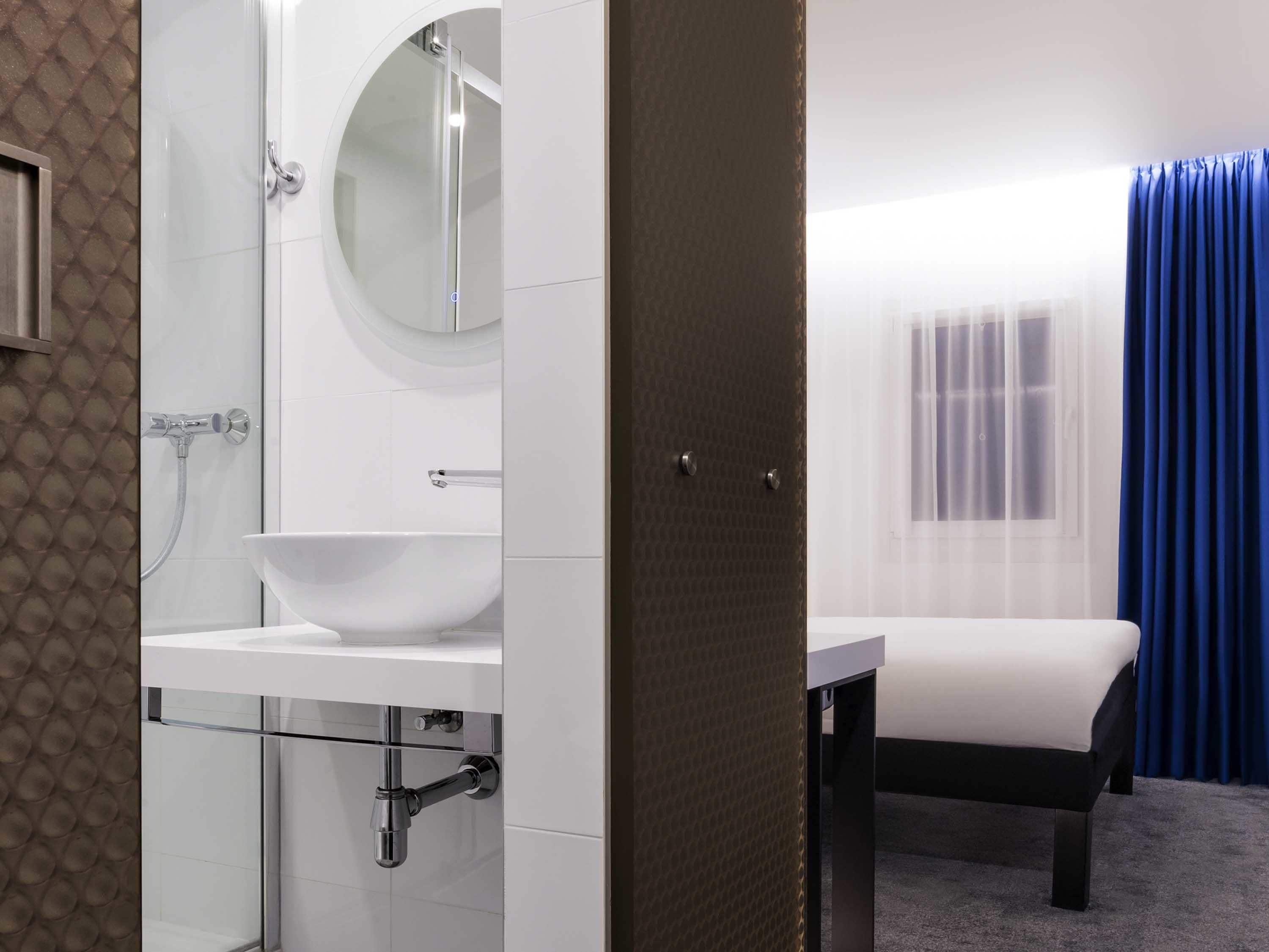 Un baño moderno con ducha de vidrio, un lavabo blanco y una mesita de noche.