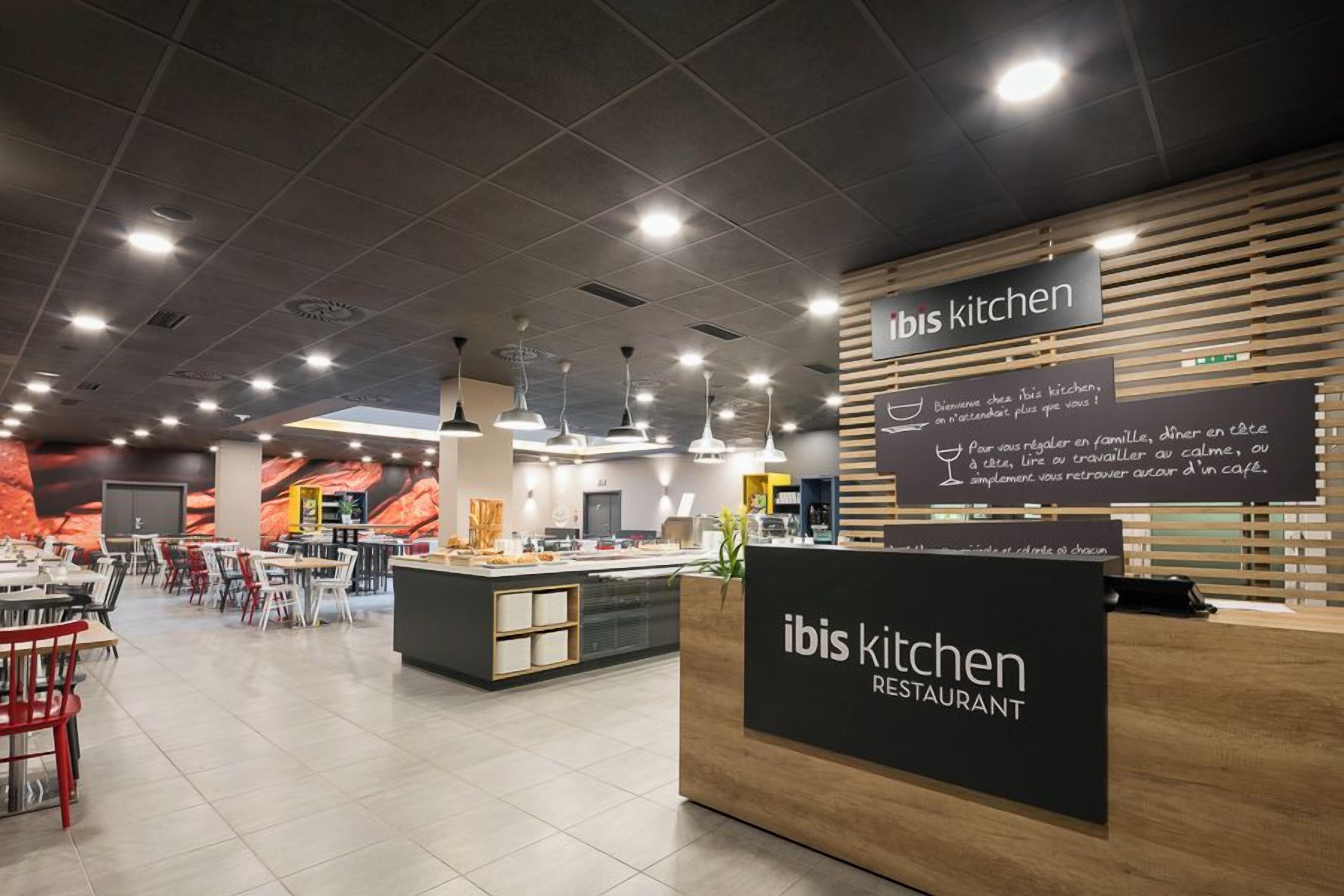 A modern restaurant interior with a central island, seating area, and a reception desk.