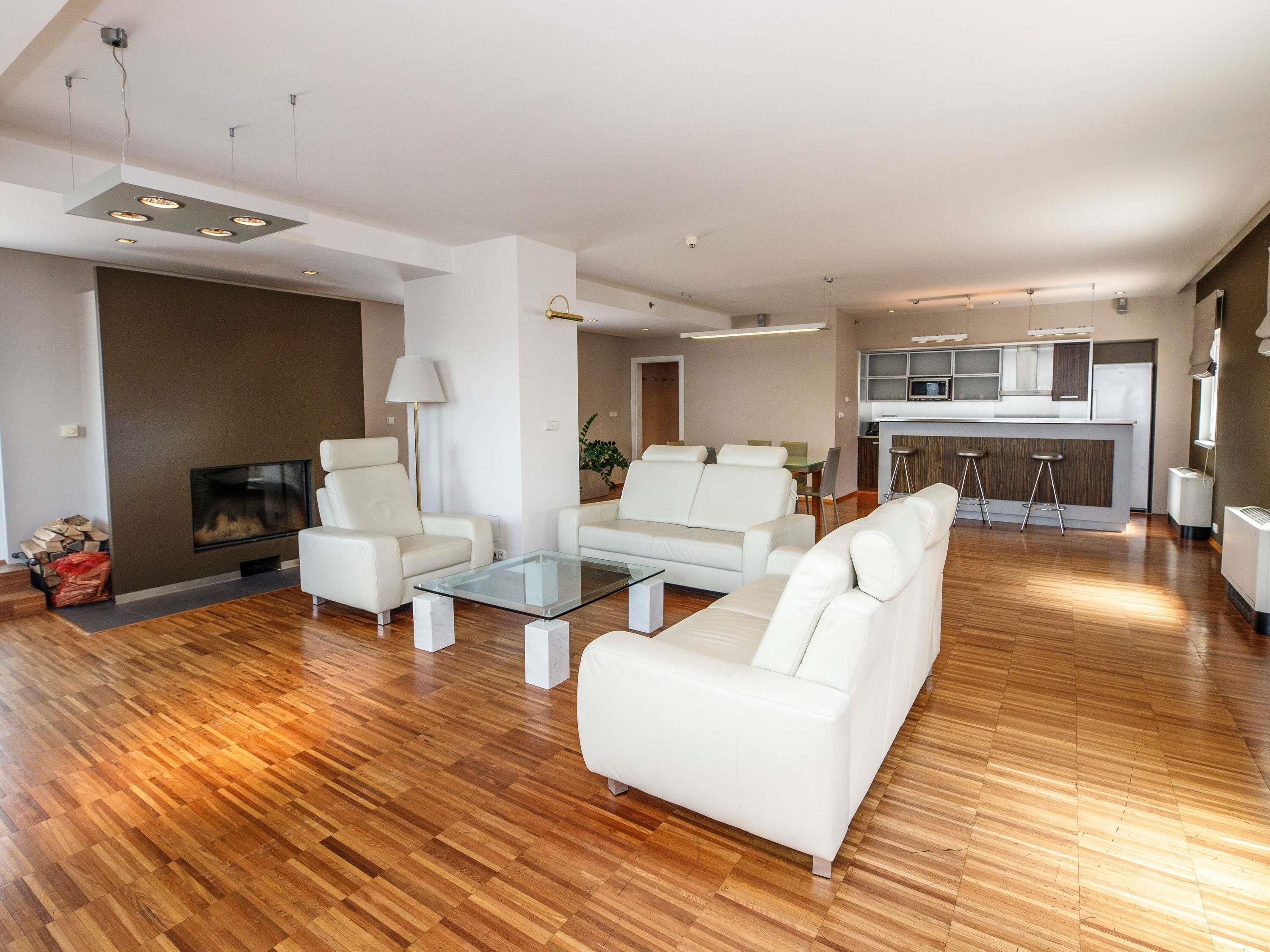 A modern living room with a fireplace, white sofas, a glass coffee table, and a kitchen area in the background.
