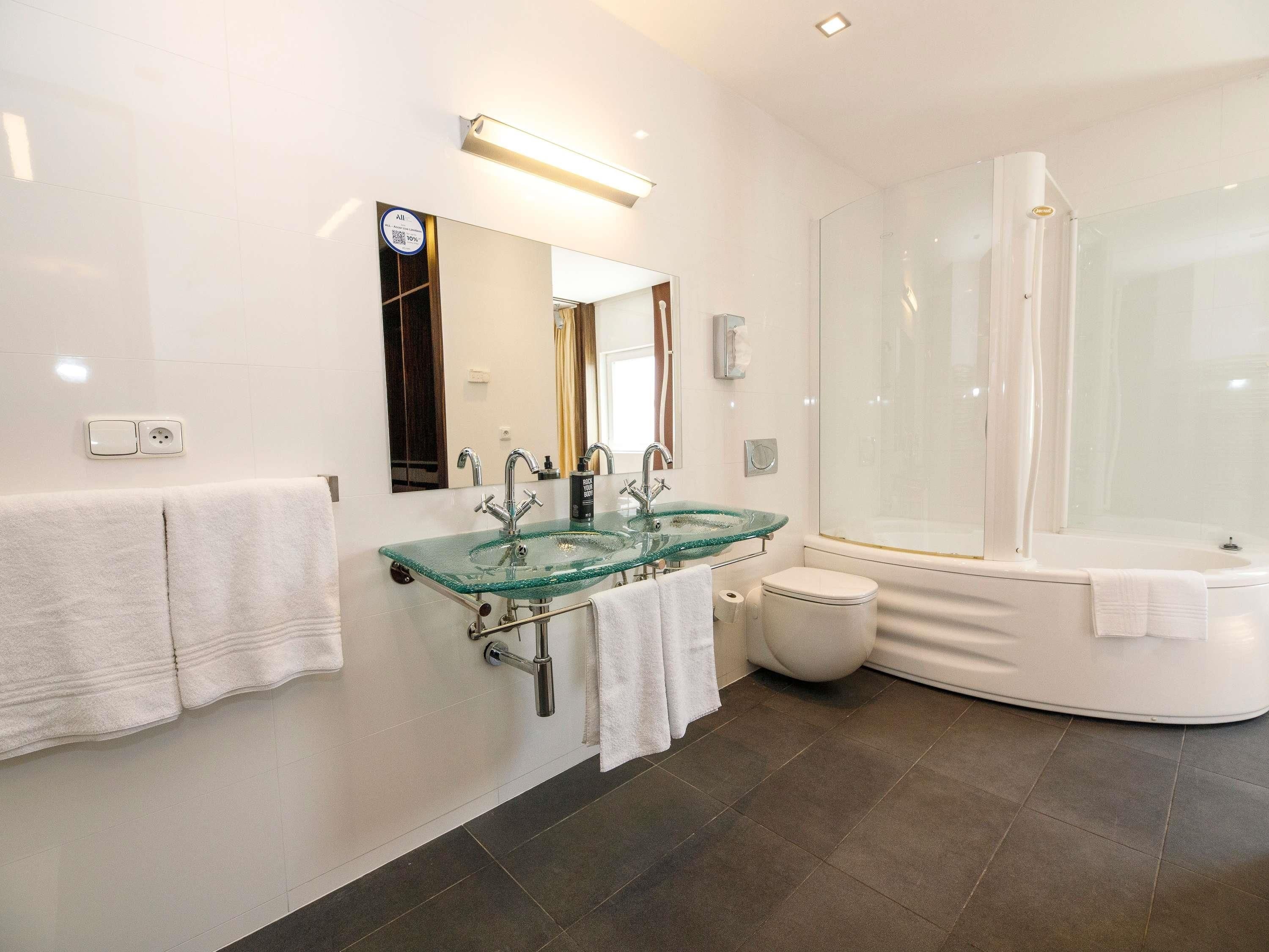 A modern bathroom with a glass sink, a large mirror, a toilet, and a separate shower area.