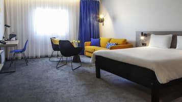Une chambre d’hôtel avec un lit, un bureau, une chaise, un canapé et une fenêtre avec des rideaux.
