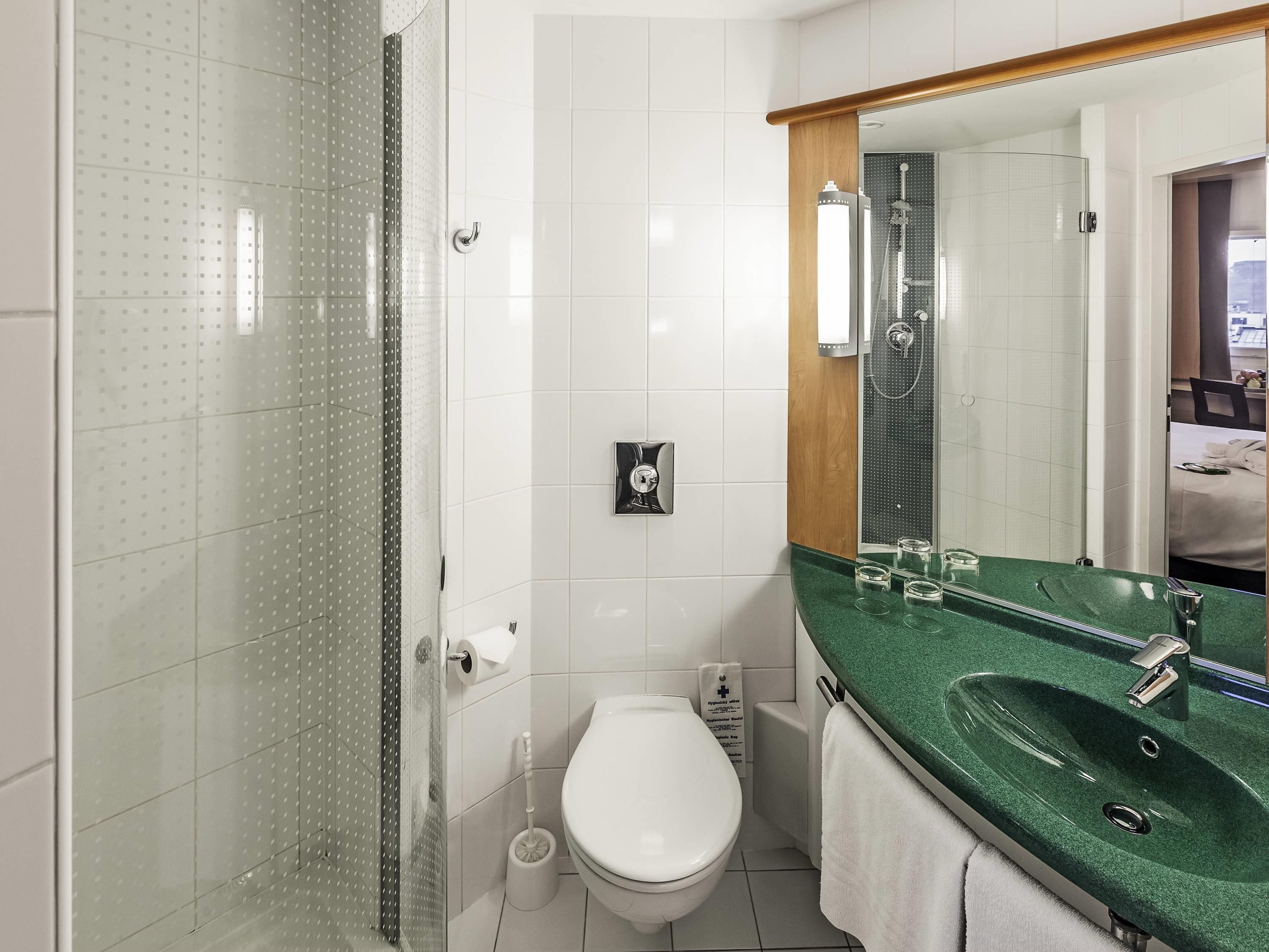 A bathroom with a glass shower enclosure, a white toilet, a green sink, and a mirror above the sink.
