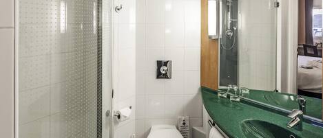 A bathroom with a glass shower enclosure, a white toilet, a green sink, and a mirror above the sink.