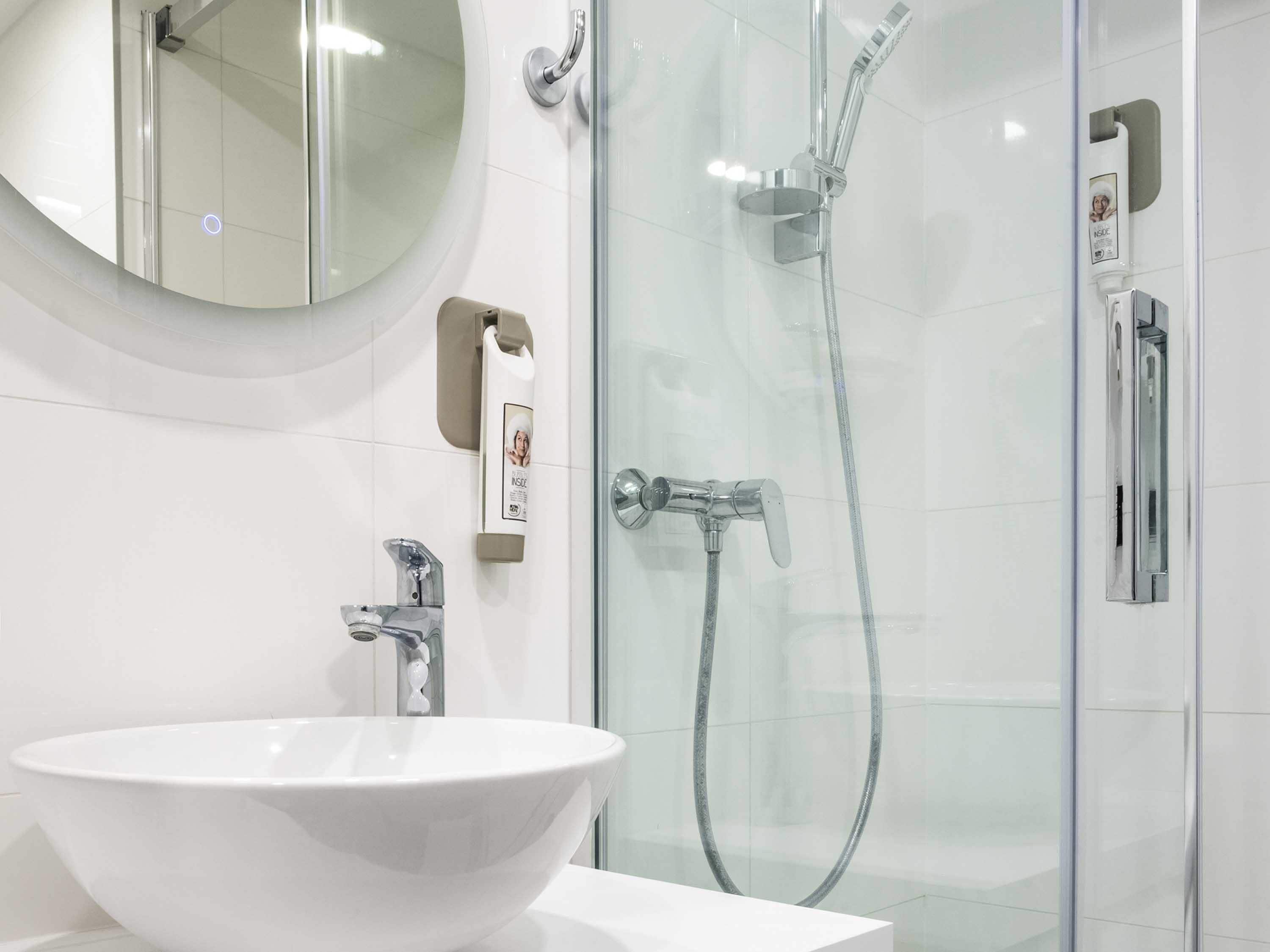 A modern bathroom with a white sink, a round mirror, a glass shower enclosure, and a handheld showerhead.
