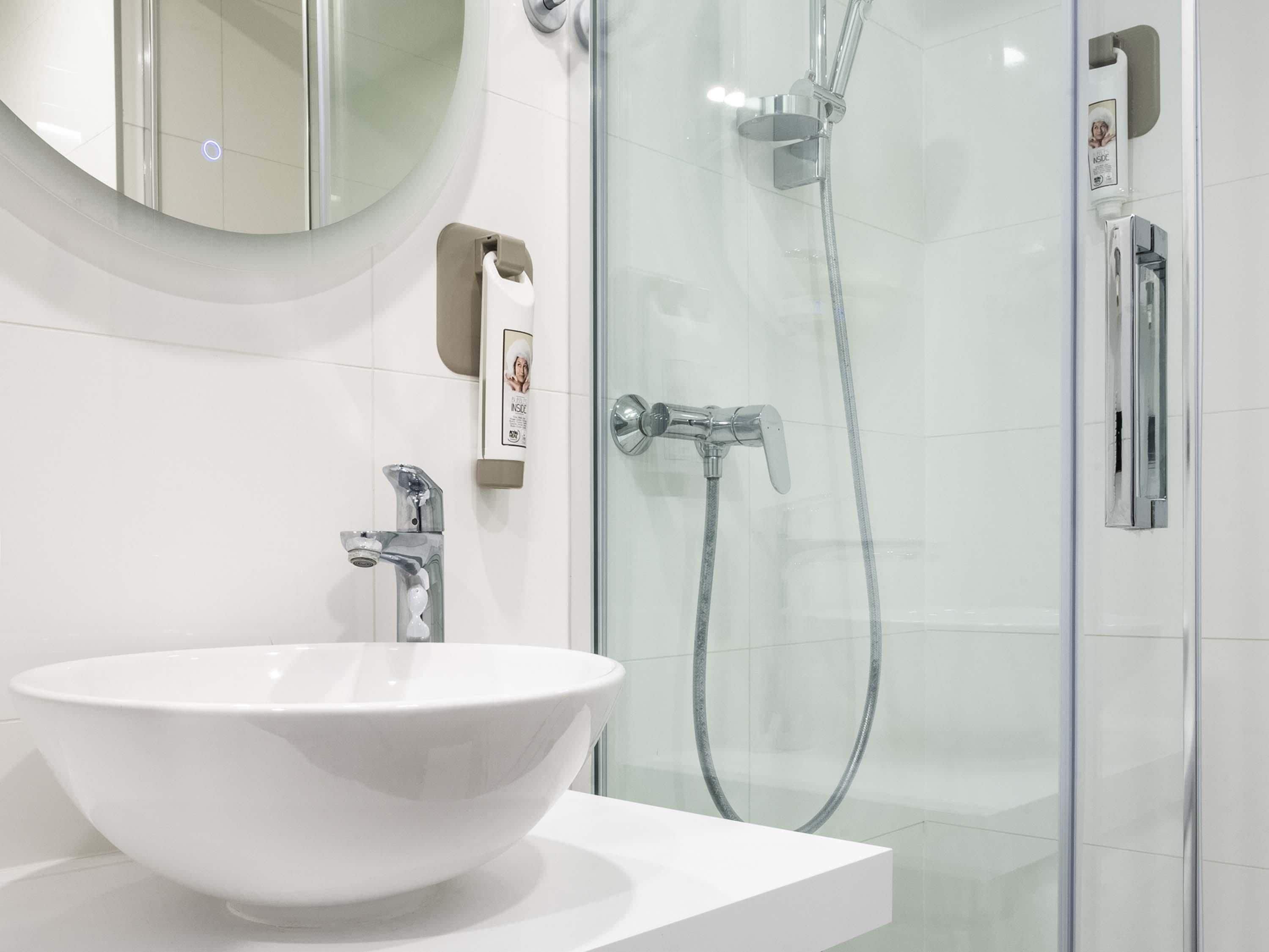 A modern bathroom with a white sink, a glass shower enclosure, and a mirror with a circular frame.