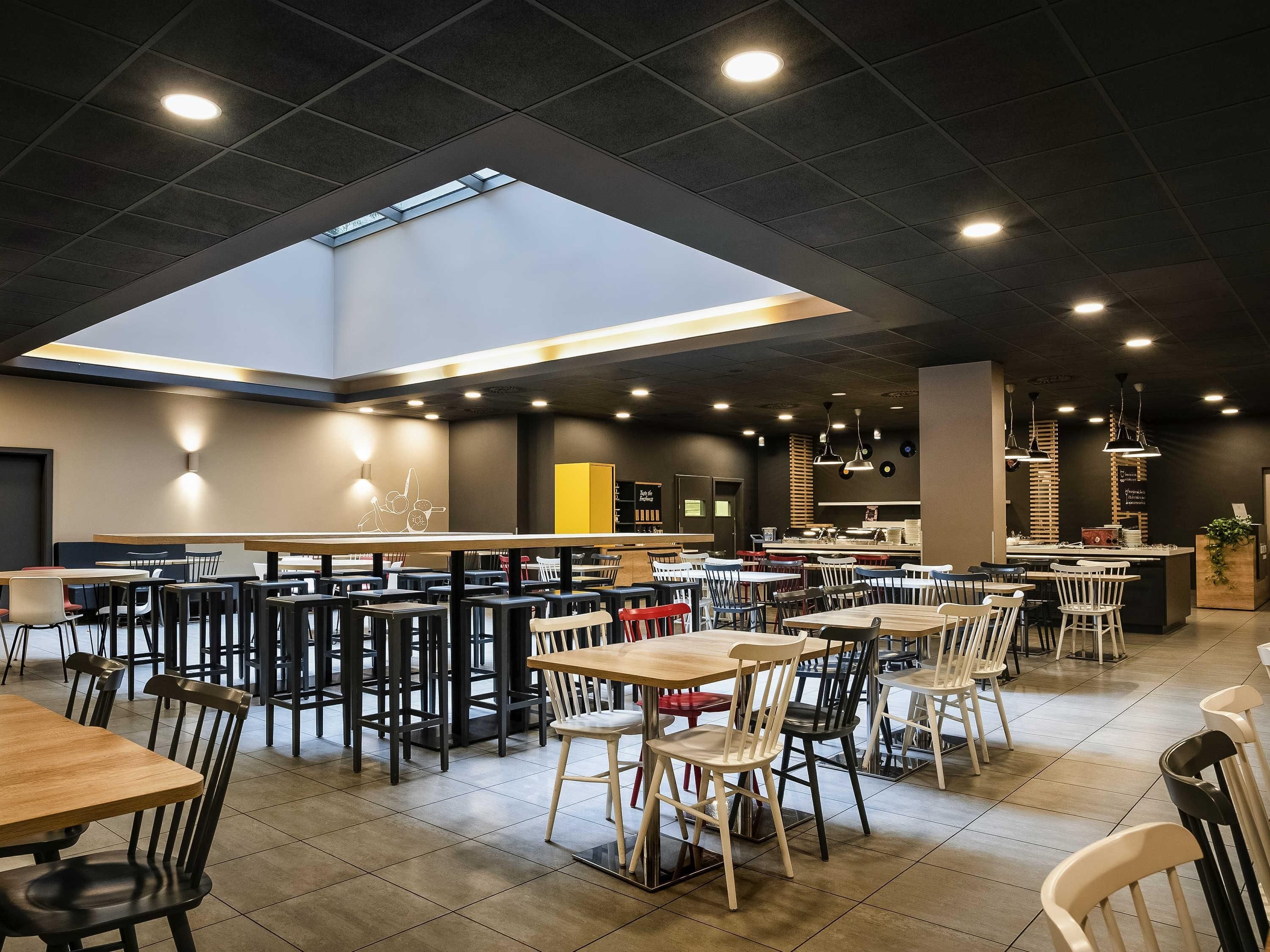 A modern restaurant with multiple dining areas, a central bar, and a skylight.