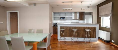 Una cocina moderna con una isla central, taburetes de bar y un comedor con una mesa de vidrio y sillas.