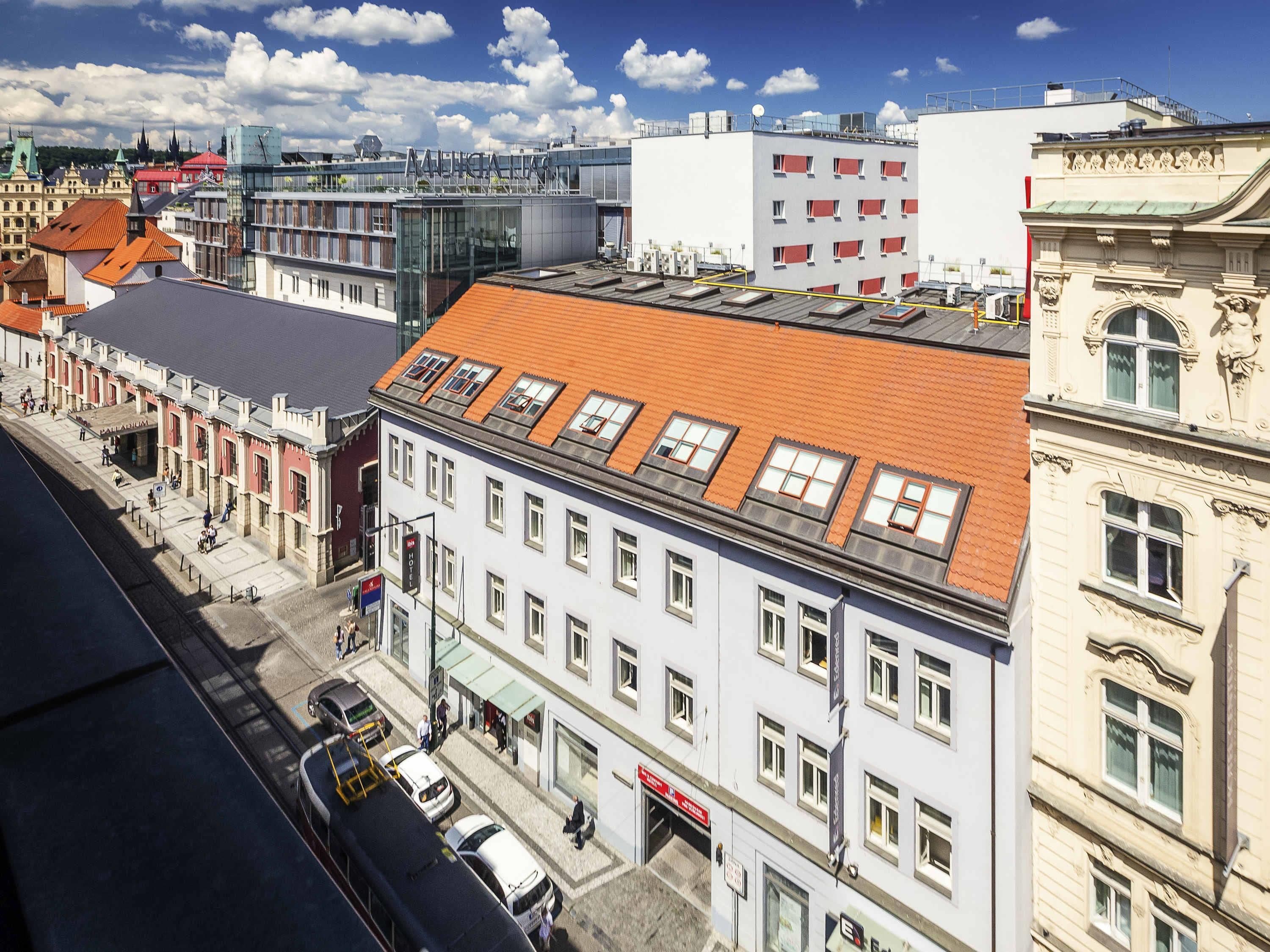 Um edifício de vários andares com telhado de telhas vermelhas, janelas amplas e uma combinação de estilos arquitetônicos, incluindo elementos tradicionais e modernos.