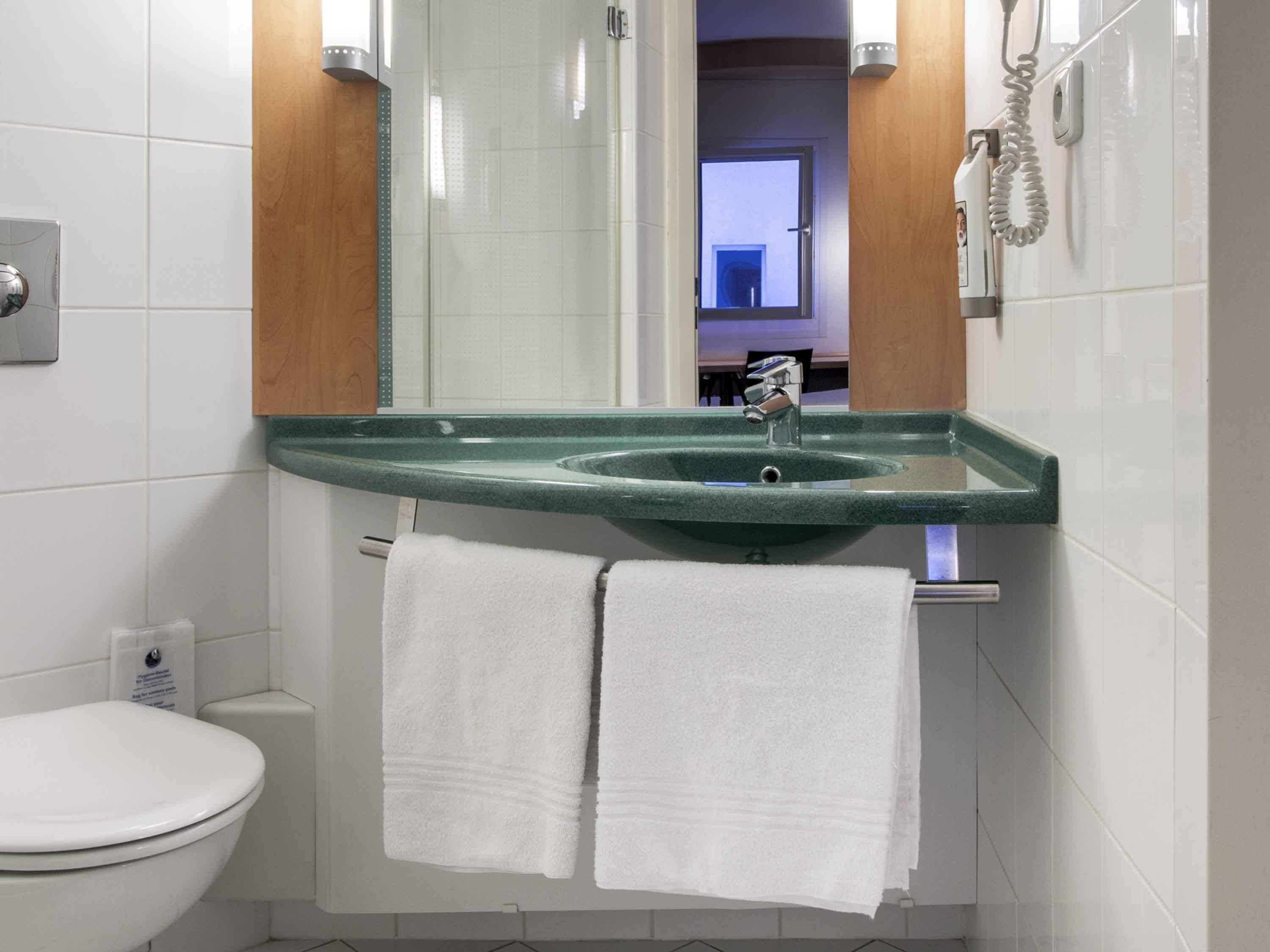 Ein Badezimmer mit Toilette in Weiß, einem grünen Waschbecken und zwei weißen Handtüchern an einem Ablagegestell.