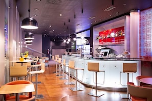A modern bar area with a curved counter, bar stools, and a seating area with tables and chairs. - ibis Praha Old Town (Prague)