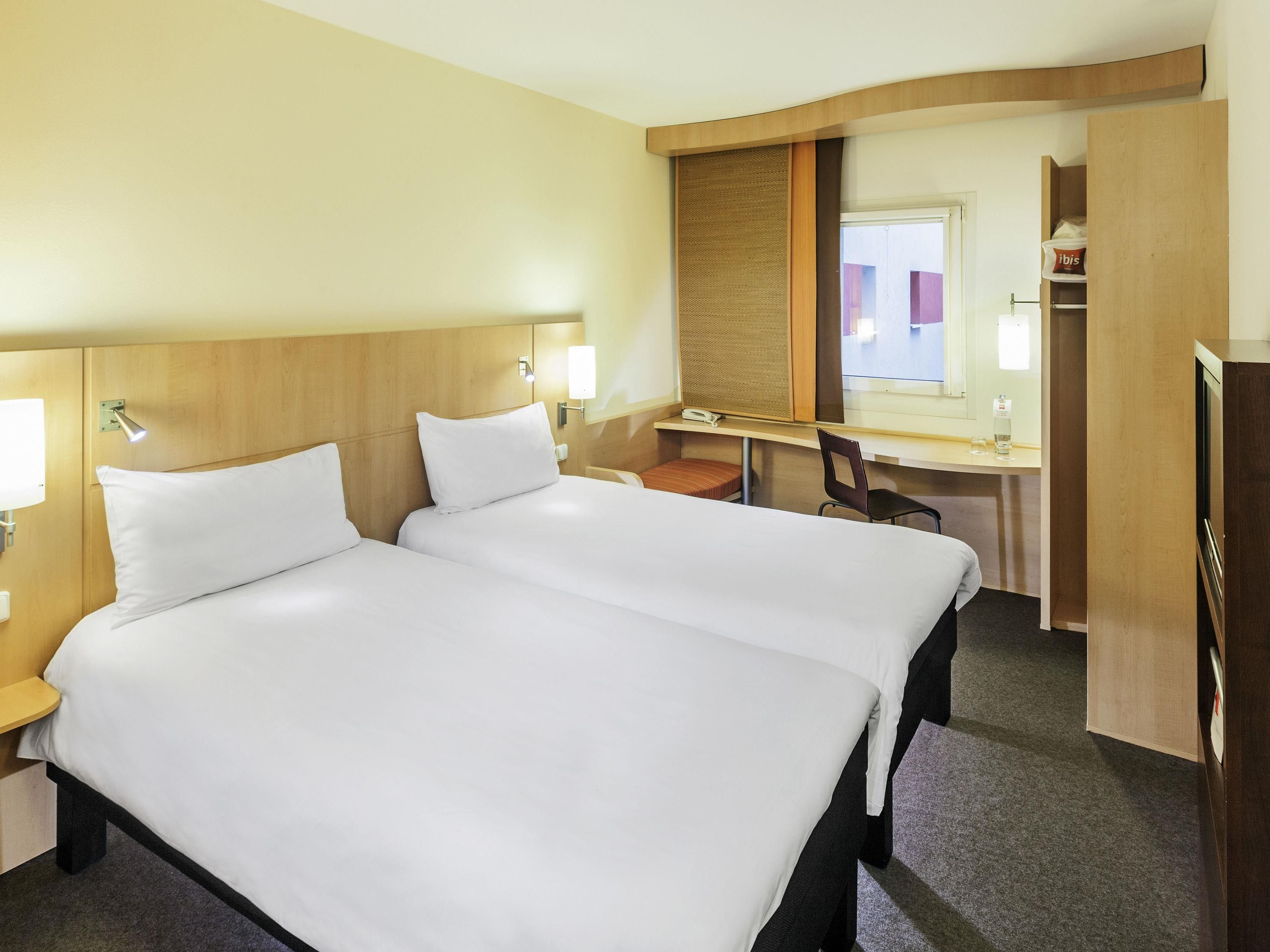 A hotel room with two beds, a desk, a chair, a mirror, and a wardrobe.