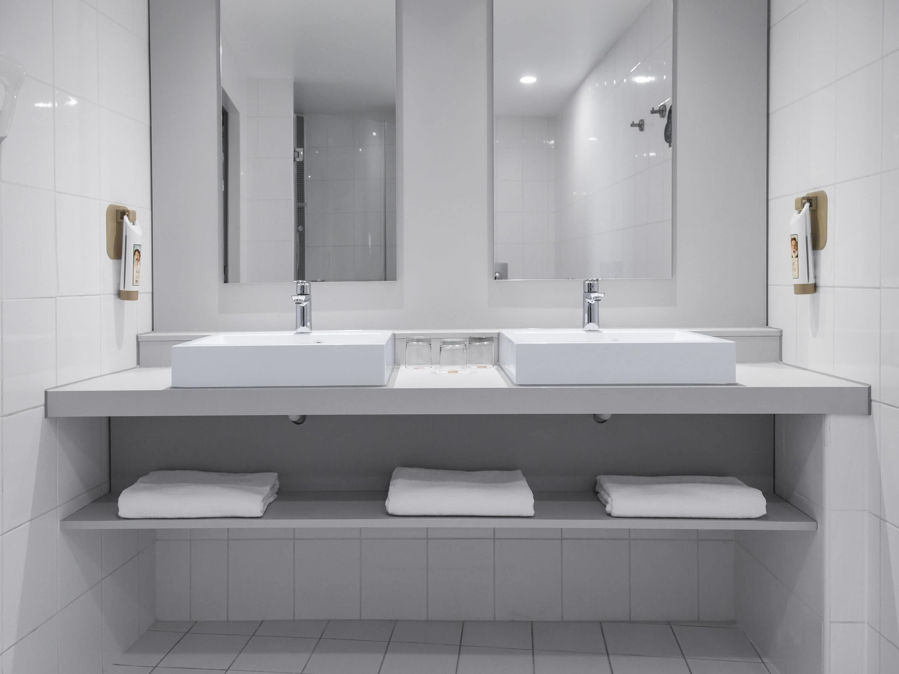 A modern bathroom with two sinks, a large mirror, and three shelves with folded towels.