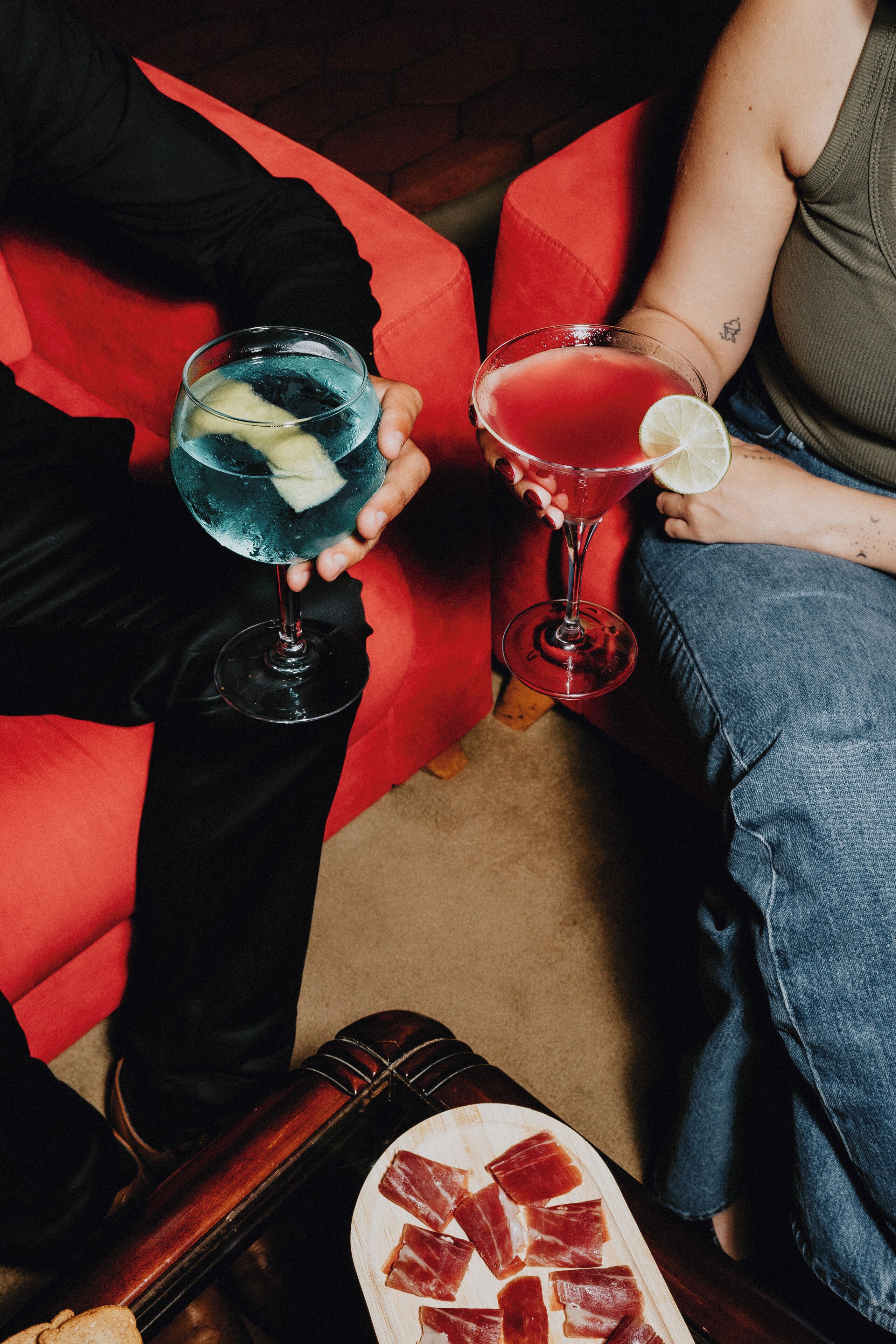 Kaksi ihmistä istuu punaisella sohvalla, ja kummallakin on kädessään cocktail-lasi.
