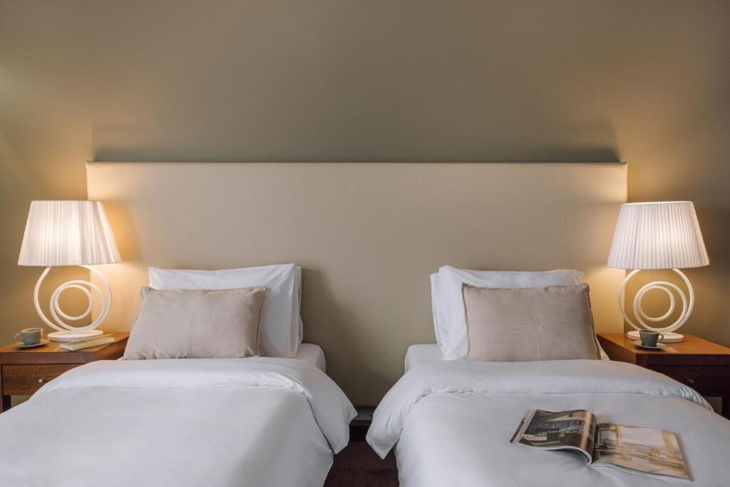 A hotel room with two beds, each with a pillow and a lamp on a bedside table.