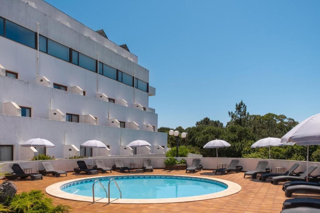 A modern hotel with a rooftop pool, multiple lounge areas with umbrellas, and a clear blue sky.