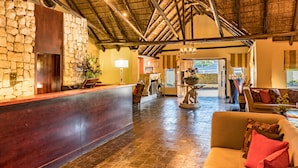 A lobby with a stone wall, wooden reception desk, and a sofa. - Shumba Valley Lodge Lanseria Airport (Lanseria)