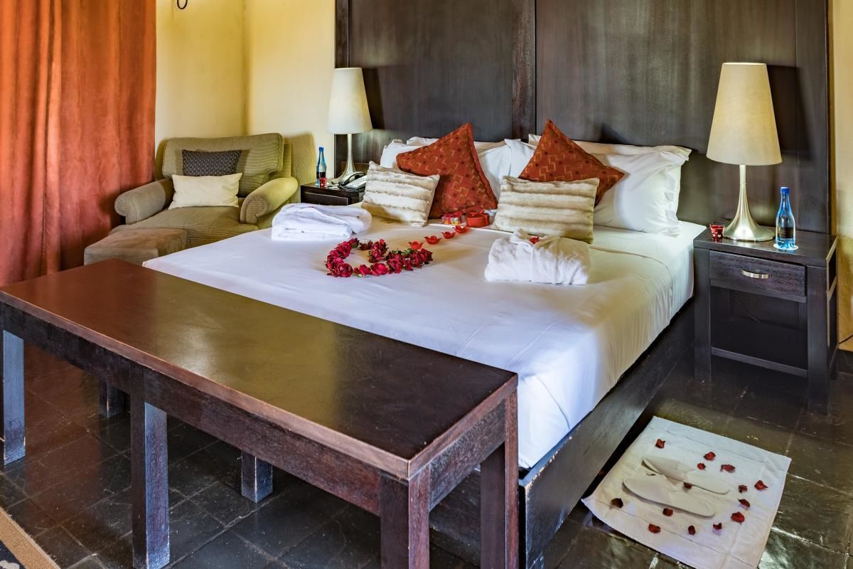 Habitación de hotel con una cama grande, una mesa de madera, un sofá, dos mesitas de noche con lámparas y una cortina roja.