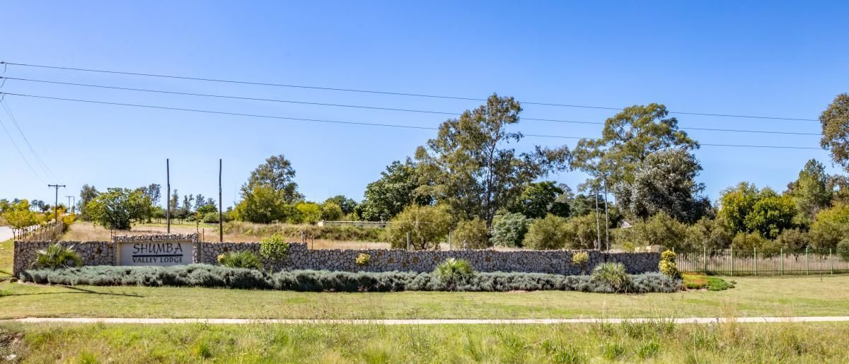 A stone wall with a sign reading "SHUMBA VALLEY LODGE" and a grassy area in front.