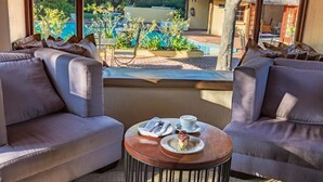 A balcony with two sofas and a small round table, overlooking a pool and garden. - Shumba Valley Lodge Lanseria Airport (Lanseria)